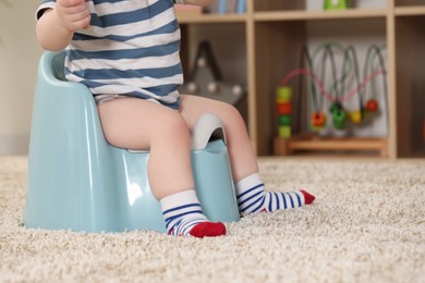 Photo of Little child sitting on plastic baby potty indoors, closeup. Space for text