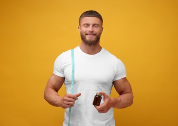 Athletic young man with measuring tape and bottle of supplements on orange background. Weight loss