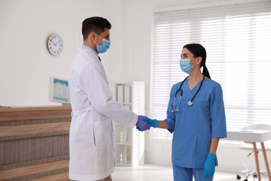 Doctors in medical gloves with protective masks giving handshake at hospital