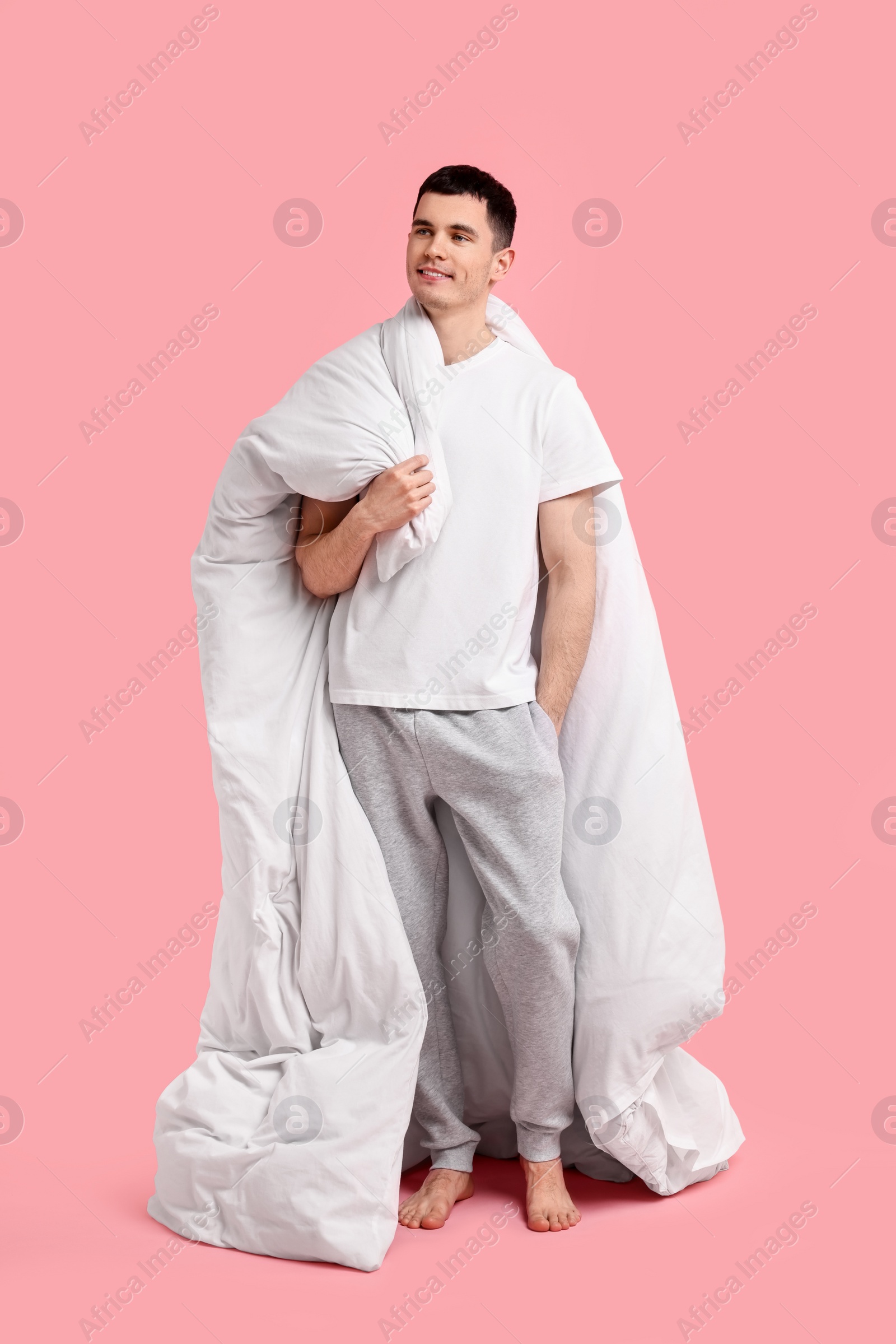 Photo of Happy man in pyjama holding blanket on pink background