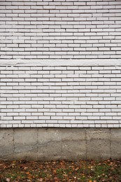 Photo of Beautiful wall made of white bricks and ground with fallen dry leaves