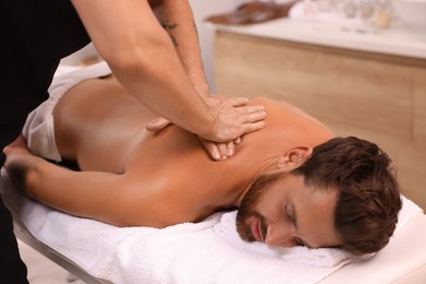 Photo of Man receiving professional back massage on couch in spa salon