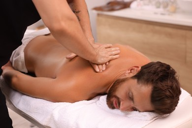 Man receiving professional back massage on couch in spa salon