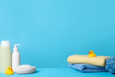 Photo of Baby cosmetic products, bath ducks, sponge and towels on light blue background. Space for text
