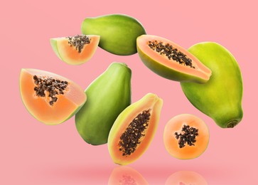 Image of Cut and whole papaya fruits falling on pink background