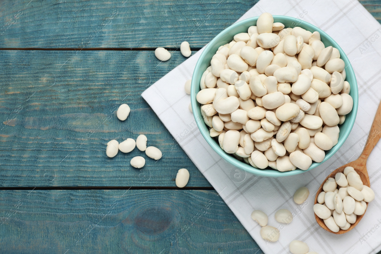 Photo of Uncooked white beans on blue wooden table, flat lay. Space for text