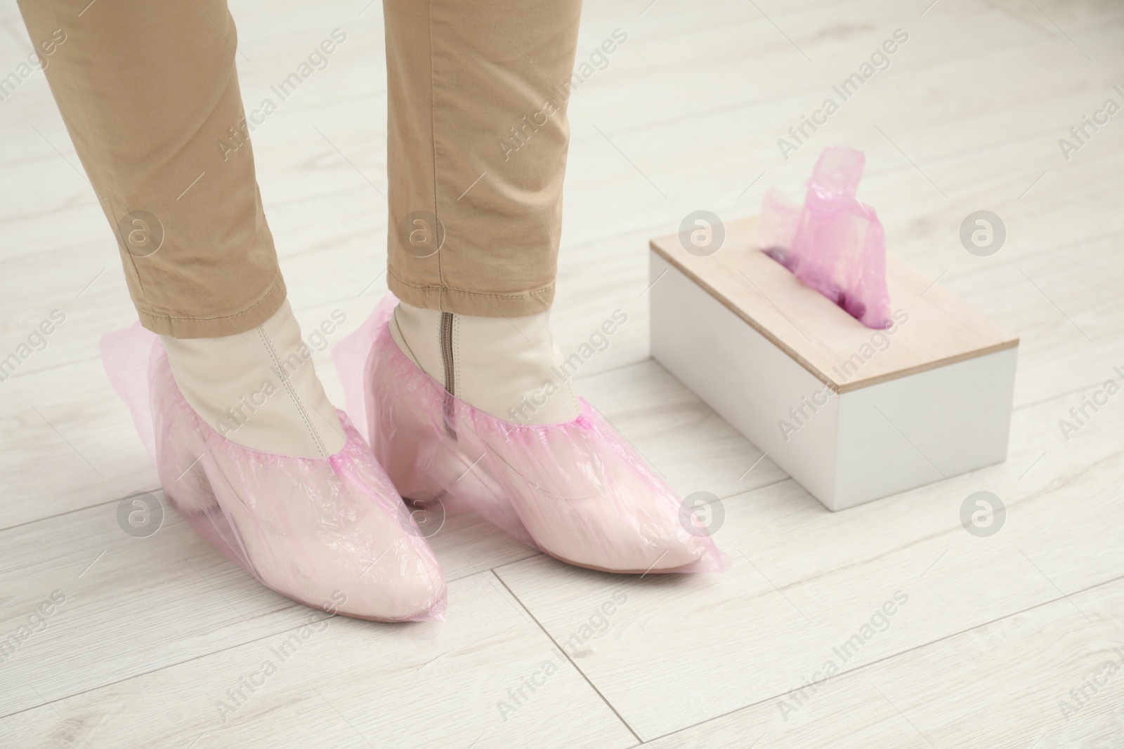 Photo of Woman wearing pink shoe covers onto her boots indoors, closeup