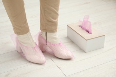 Woman wearing pink shoe covers onto her boots indoors, closeup