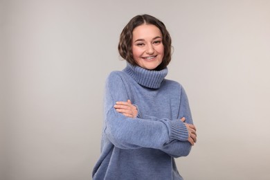 Smiling woman with dental braces in warm sweater on grey background