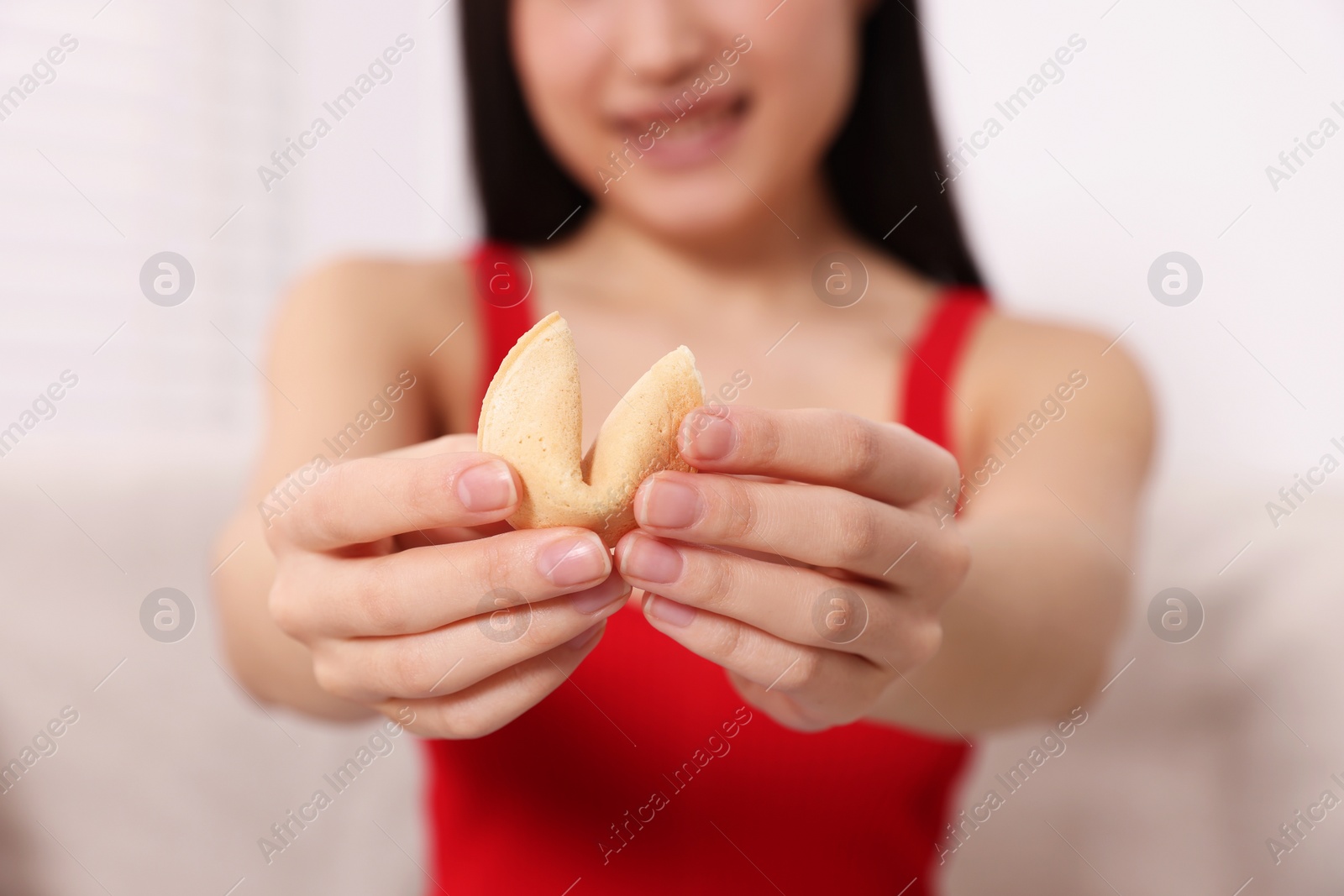 Photo of Young woman holding tasty fortune cookie with prediction indoors, closeup