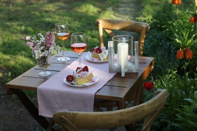 Vase with spring flowers, wine and cake on table served for romantic date in garden