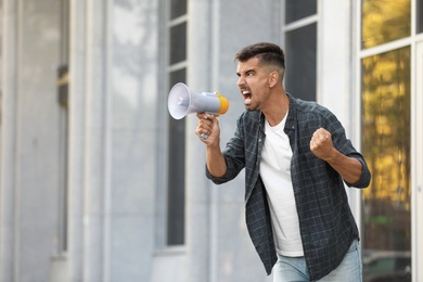 Image of Emotional young man with megaphone outdoors. Protest leader