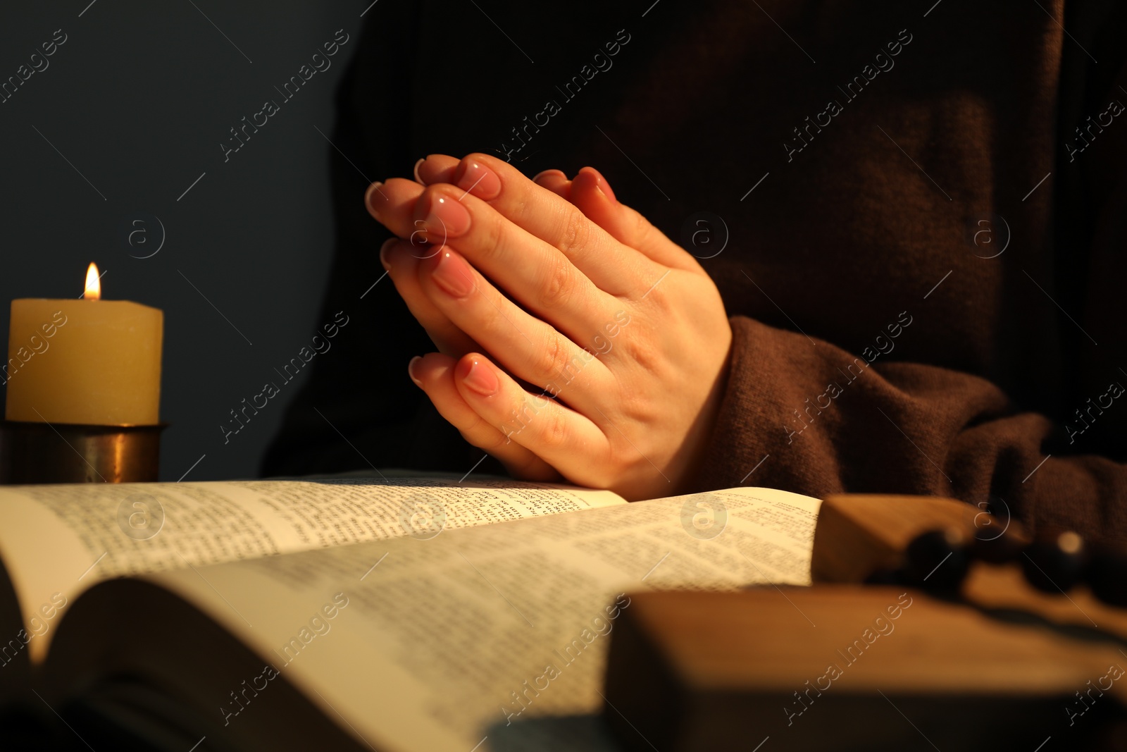 Photo of Woman praying at table with burning candle and Bible, closeup