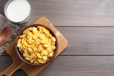 Photo of Tasty crispy corn flakes and glass of milk on wooden table, flat lay. Space for text