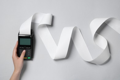 Photo of Woman using payment terminal with thermal paper for receipt on light grey background, top view