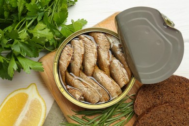 Canned sprats, herbs, bread and lemon on white wooden table, flat lay