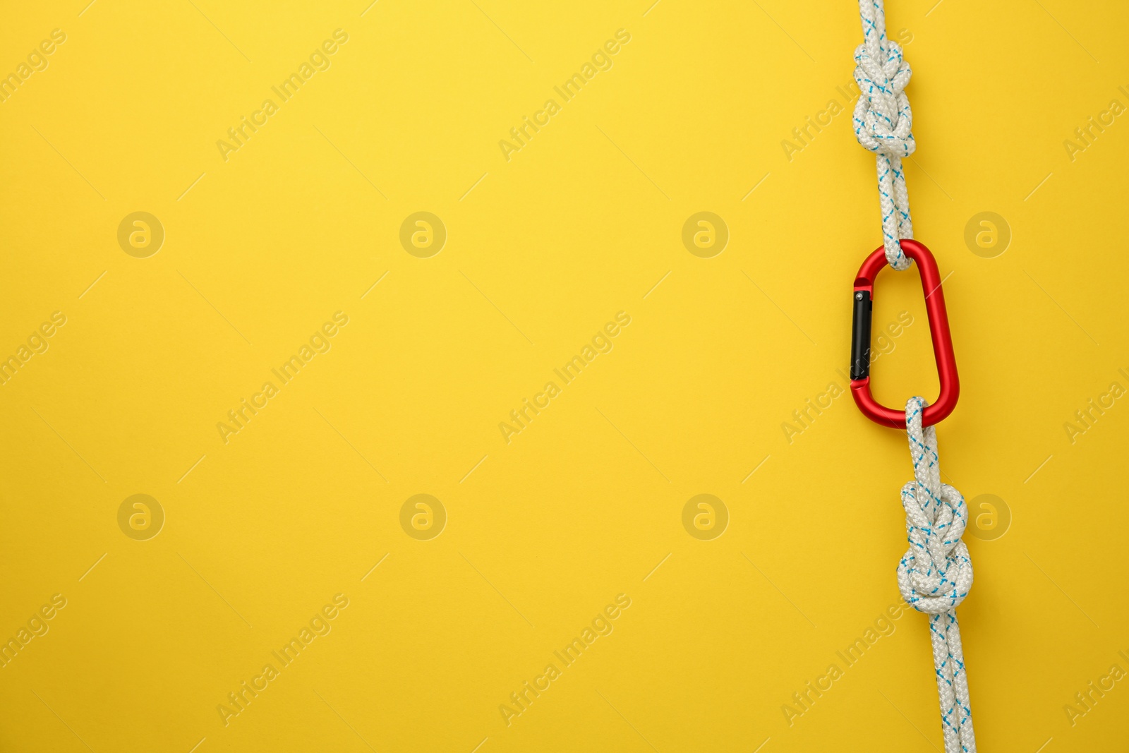 Photo of One metal carabiner with ropes on yellow background, top view. Space for text