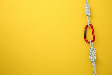 One metal carabiner with ropes on yellow background, top view. Space for text