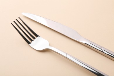 Photo of Stylish cutlery. Silver knife and fork on beige background, closeup