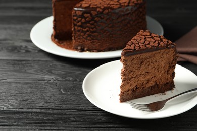 Photo of Piece of delicious chocolate truffle cake and fork on black wooden table, closeup. Space for text