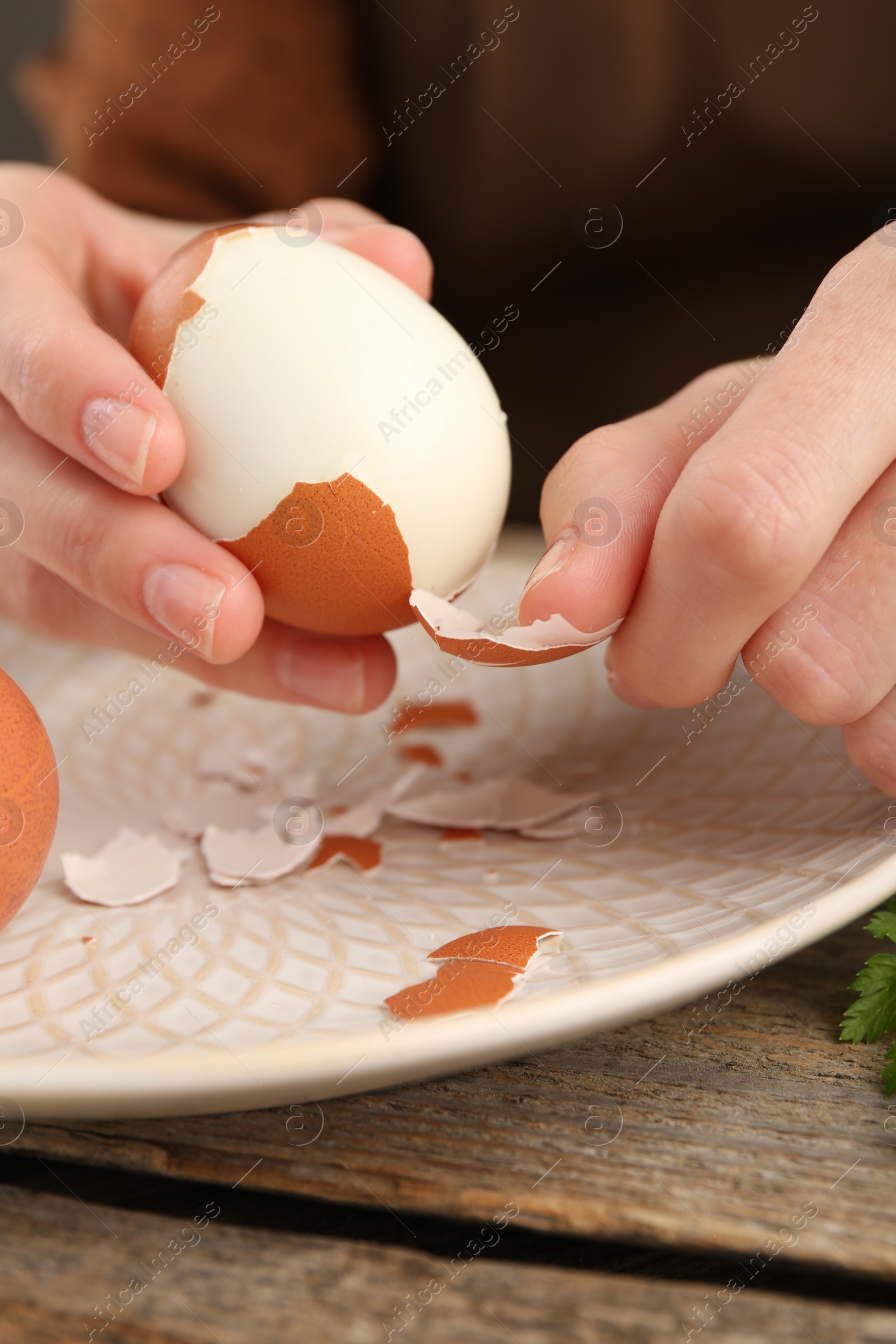 Photo of Woman peeling boiled egg at wooden table, closeup