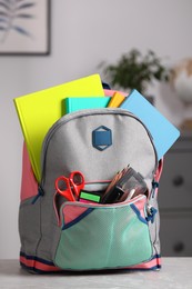 Children's backpack with different school stationery on table indoors