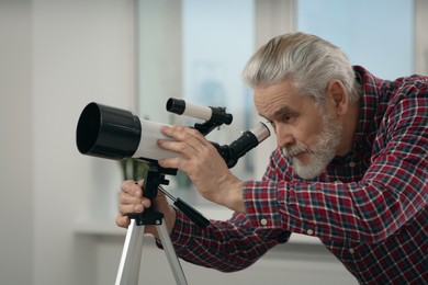 Photo of Senior man looking at stars through telescope in room