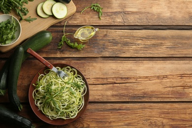 Photo of Tasty zucchini pasta with arugula and ingredients on wooden table, flat lay. Space for text
