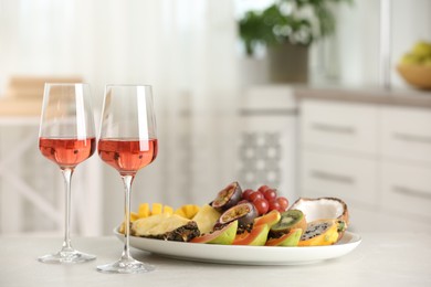 Delicious exotic fruits and glasses of wine on white table indoors