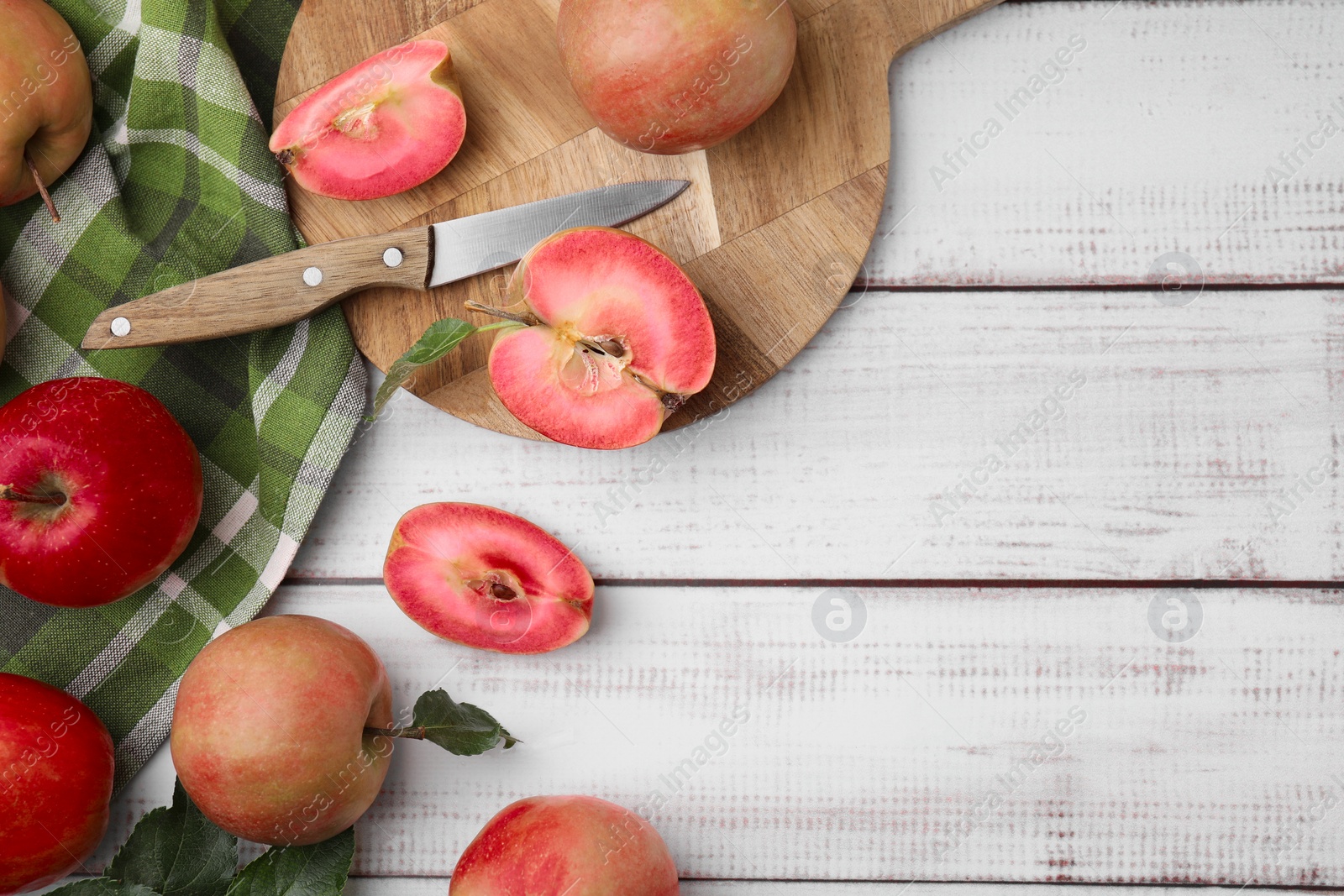 Photo of Tasty apples with red pulp and leaves on white wooden table, flat lay. Space for text