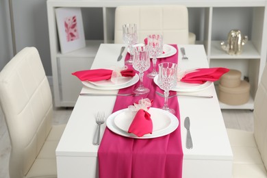 Photo of Color accent table setting. Glasses, plates, cutlery and pink napkins in dining room