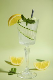 Photo of Glass of tasty fresh cucumber water with mint and sliced lemon on light green background