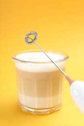 Mini mixer (milk frother) and tasty cappuccino in glass on yellow background