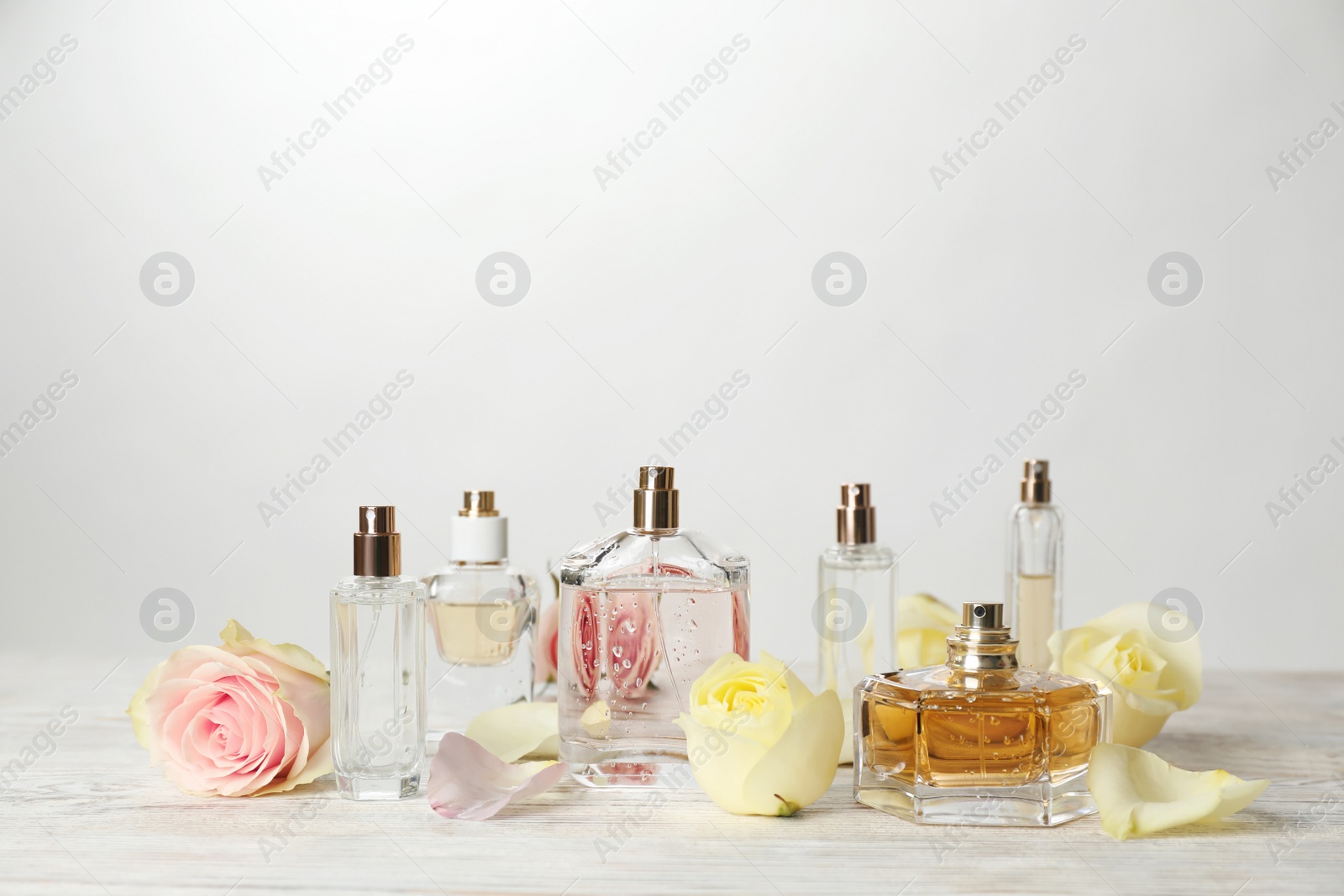 Photo of Bottles of perfume and flowers on table against light background