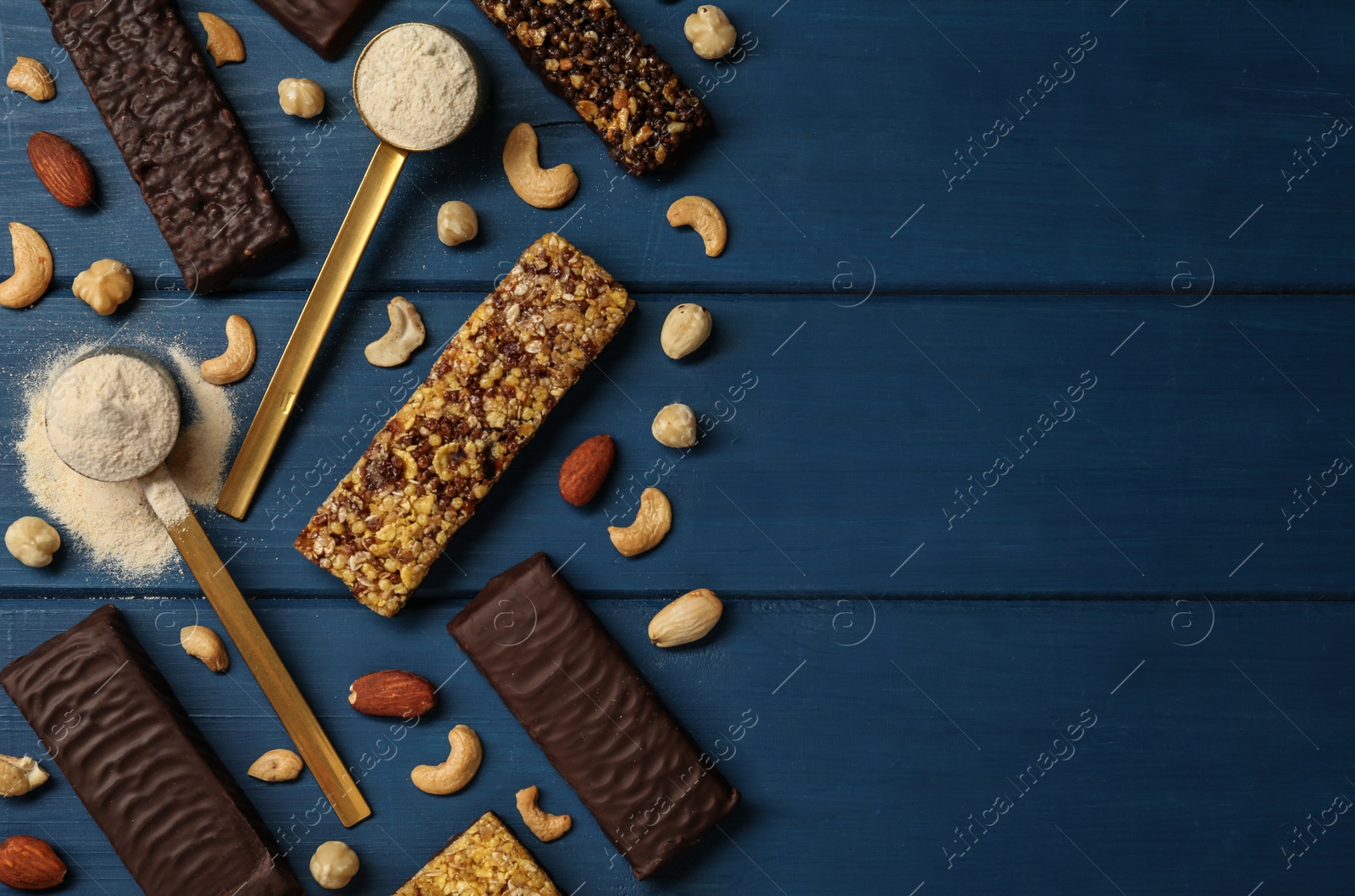 Photo of Different tasty bars, nuts and protein powder on blue wooden table, flat lay. Space for text