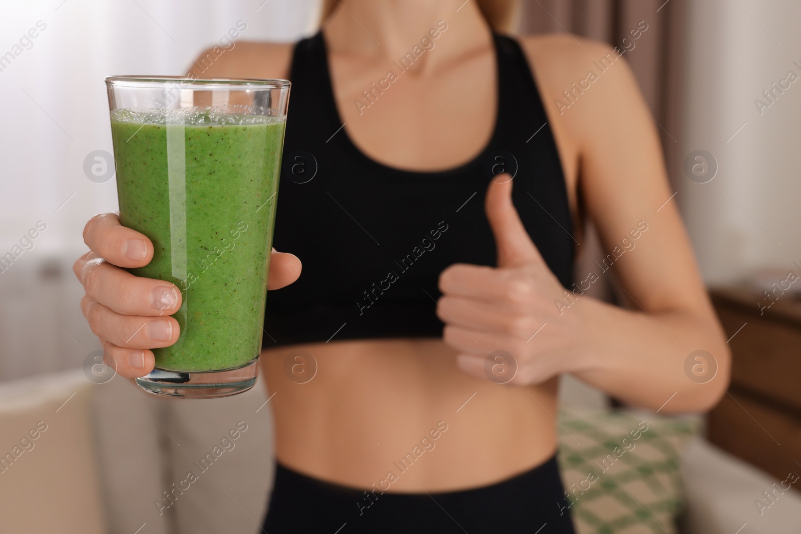 Photo of Young woman in sportswear with glass of fresh smoothie at home, closeup