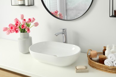 Photo of Vase with beautiful pink tulips and toiletries near sink in bathroom