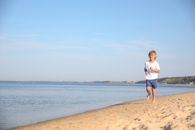 Photo of Cute little child running at sandy beach on sunny day