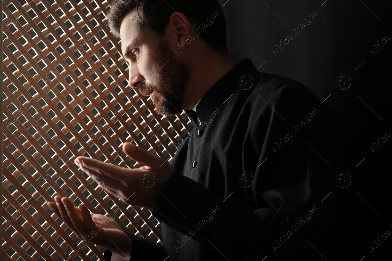 Photo of Catholic priest in cassock talking to parishioner in confessional