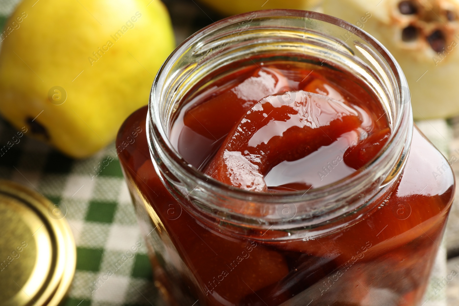 Photo of Tasty homemade quince jam in jar and fruits on table, closeup