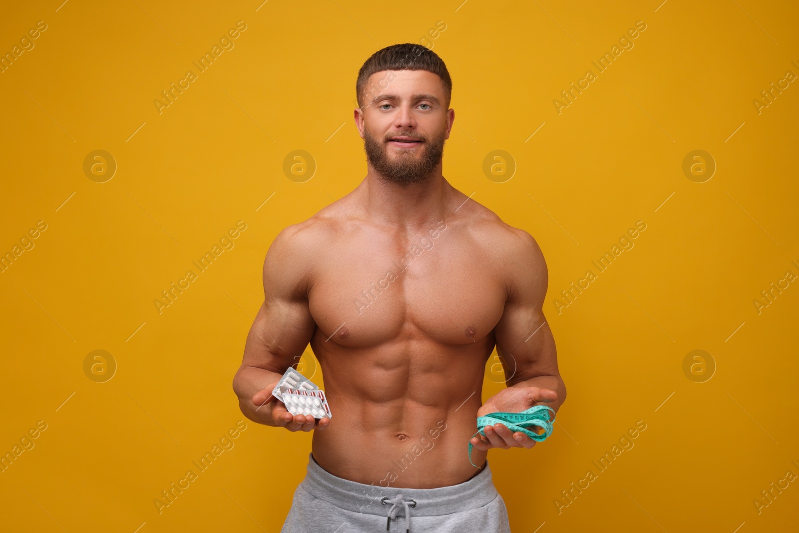 Photo of Athletic young man with measuring tape and pills on orange background. Weight loss