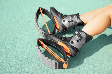 Photo of Woman with kangoo jumping boots on turquoise textured background, closeup