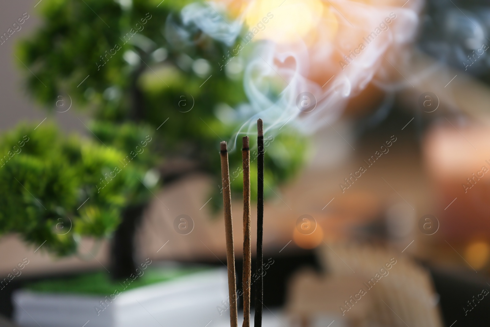 Photo of Incense sticks smoldering on blurred background, closeup