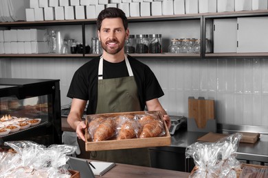 Photo of Happy seller with croissants at cashier desk in bakery shop