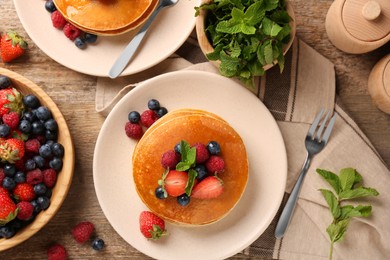 Tasty pancakes with fresh berries and mint on wooden table, flat lay