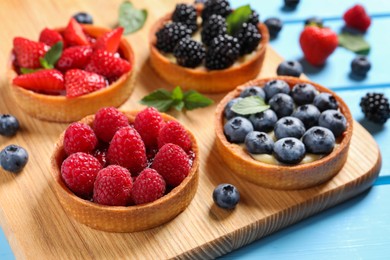 Photo of Tartlets with different fresh berries on light blue table, closeup. Delicious dessert