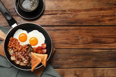 Photo of Frying pan with cooked traditional English breakfast and cup of coffee on wooden table, flat lay. Space for text
