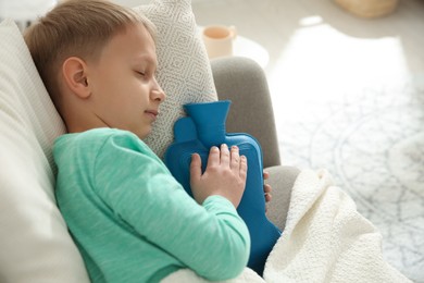 Photo of Ill boy with hot water bottle suffering from cold at home