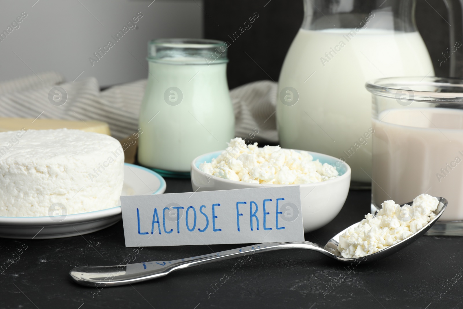 Photo of Many different dairy products and card with phrase Lactose free on black textured table, closeup