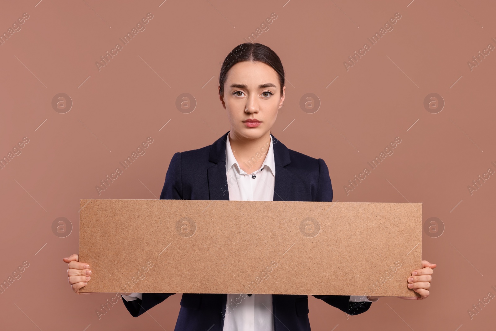 Photo of Young woman holding blank cardboard banner on brown background, space for text